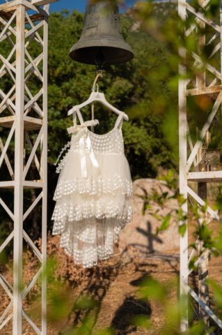 The first dress of a baby girl, after becoming a christian, is hanging from a bell. At the background we see the shadow of a cross.